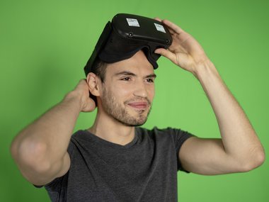Mann, der eine VR-Brille trägt, steht vor einem grünen Hintergrund
