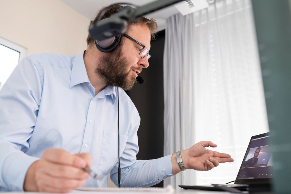Man wearing headphones, participating in a video conference and facing his laptop