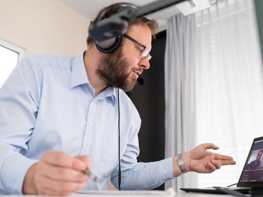 Man wearing headphones, participating in a video conference and facing his laptop