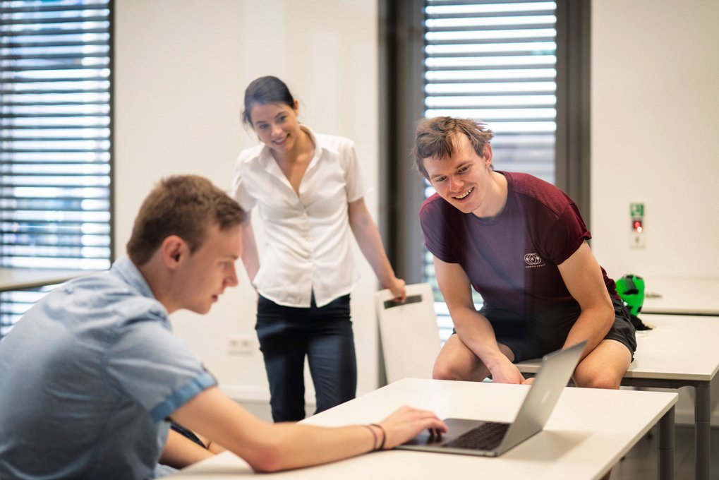 Three people in a classroom looking at a laptop together